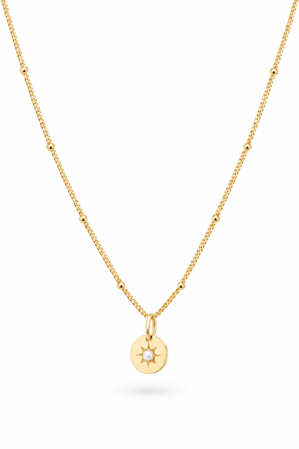 A delicate gold chain necklace featuring a small circular pendant with a sunburst design and a tiny seed pearl in the center, displayed against a clean white background.