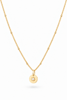 A delicate gold chain necklace featuring a small circular pendant with a sunburst design and a tiny seed pearl in the center, displayed against a clean white background.