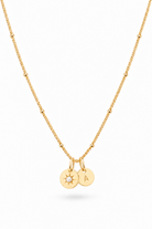 A delicate gold chain necklace featuring two small round charms: one solid gold stamped with the letter 'A' and the other with a sunburst design, displayed on a clean white background.