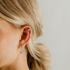 A Petite Vintage Pearl Stud is worn in the cartilage of a woman's ear and sits above a Petite Daisy Stud. 