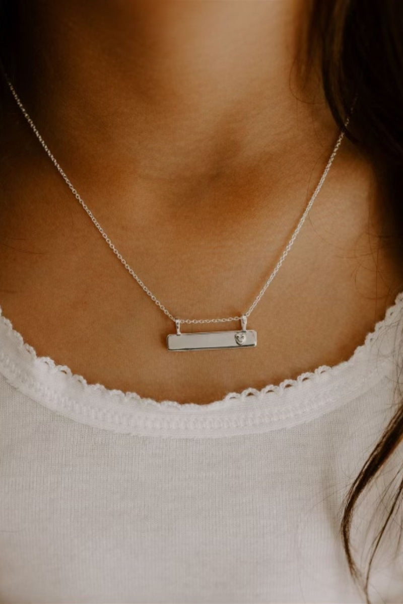 Child wearing Darling Bar Necklace in silver with heart engraving. 
