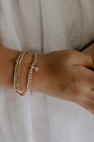 A Signature Bracelet is worn alongside a cuban link bracelet with a daisy pendant on it