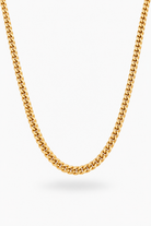 A close-up of a gold-toned curb chain necklace draped in a U-shape against a clean white background.