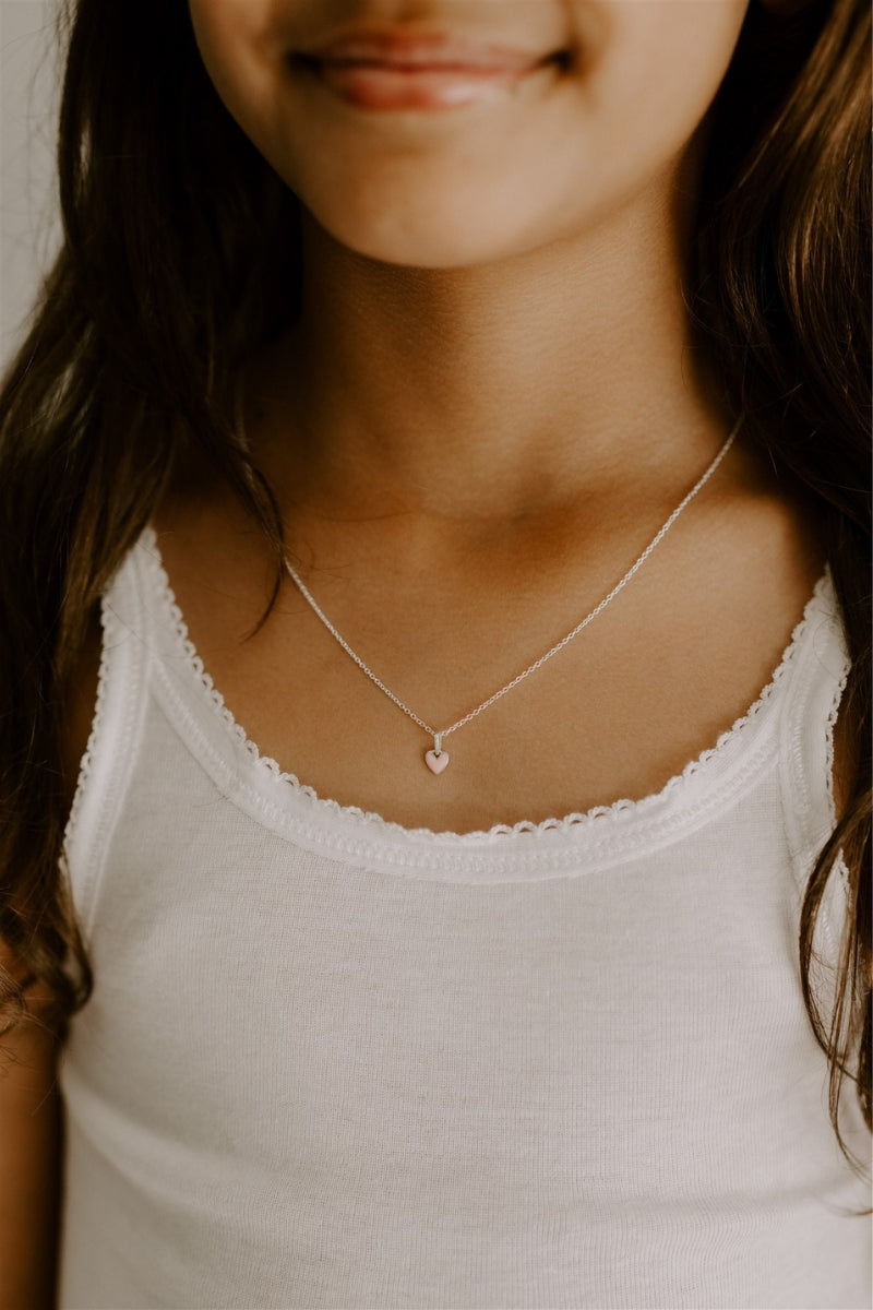 The Pink Petite Darling necklace with its soft pink heart pendant on a fine cable chain is worn by a young girl.