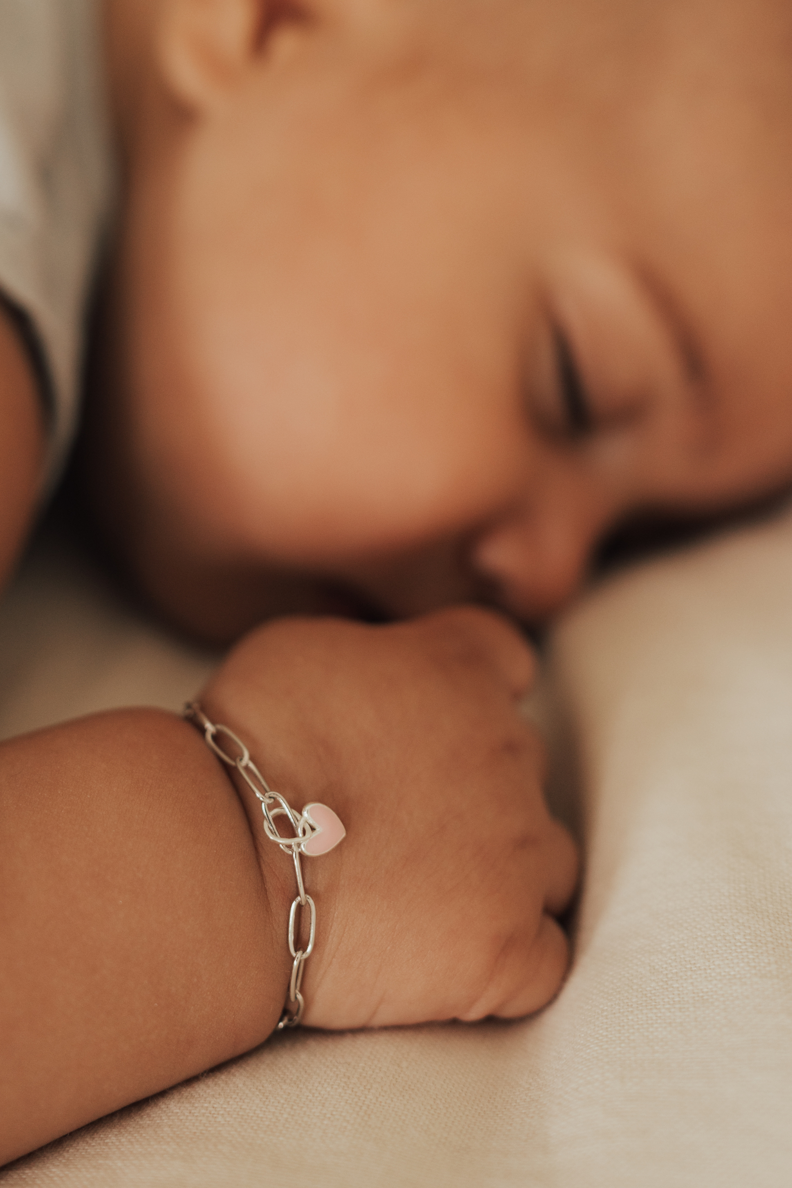 Sleeping baby wearing Darling Posie Bracelet with pink heart charm on silver link chain by Bluebird Jewellery