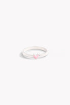 A silver ring with a classic band design and a pink heart-shaped embellishment on the top.