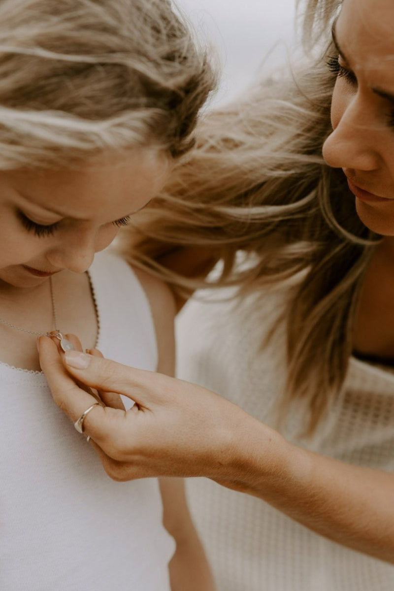 Delicate silver necklace with engraved pendant, worn close to heart as a meaningful keepsake for women.
