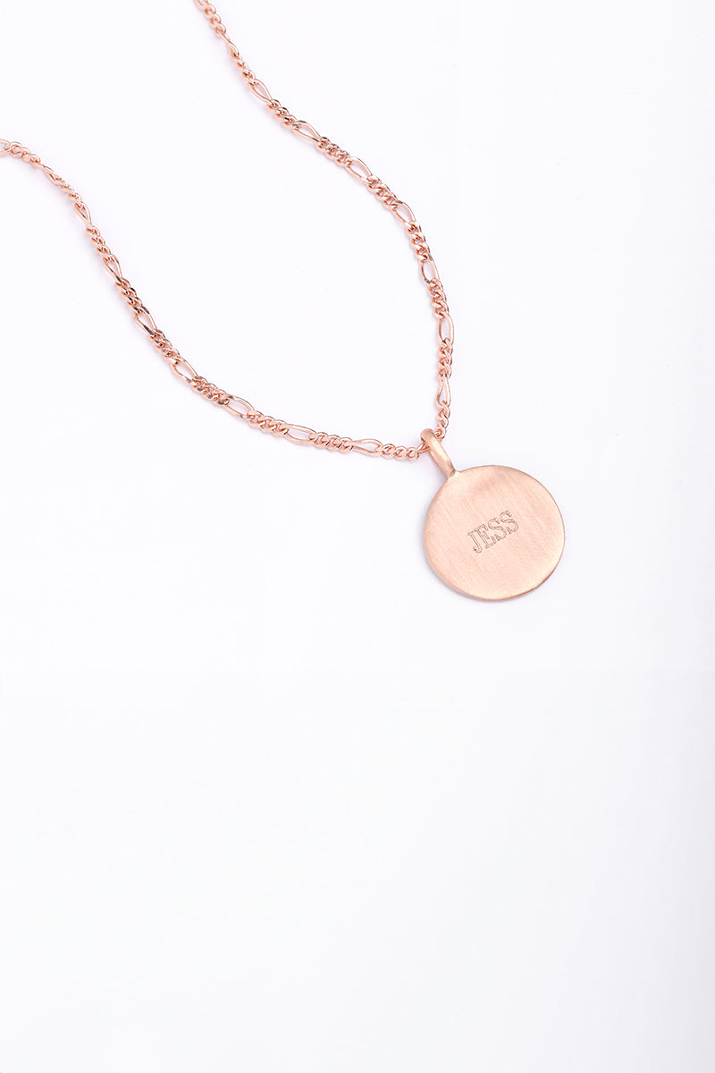 Rose gold disc necklace engraved with ‘JESS’, photographed flat with Figaro chain