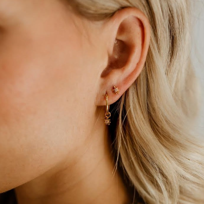 A Petite Daisy Hoop is worn alongside a Petite Daisy Stud in a woman's earlobe.  The matching Daisies complimenting one another.