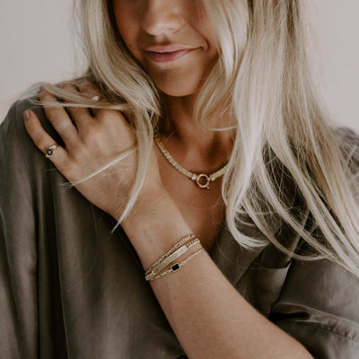 A woman is wearing her Gold Signature Bracelet with a Loved Bracelet and Figaro Bracelet as well as a dainty Pinky Ring made from solid 9ct gold.