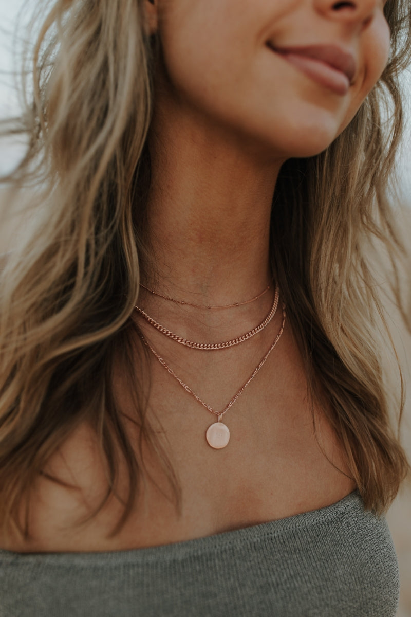 Woman wearing rose gold disc necklace layered with fine rose gold chains