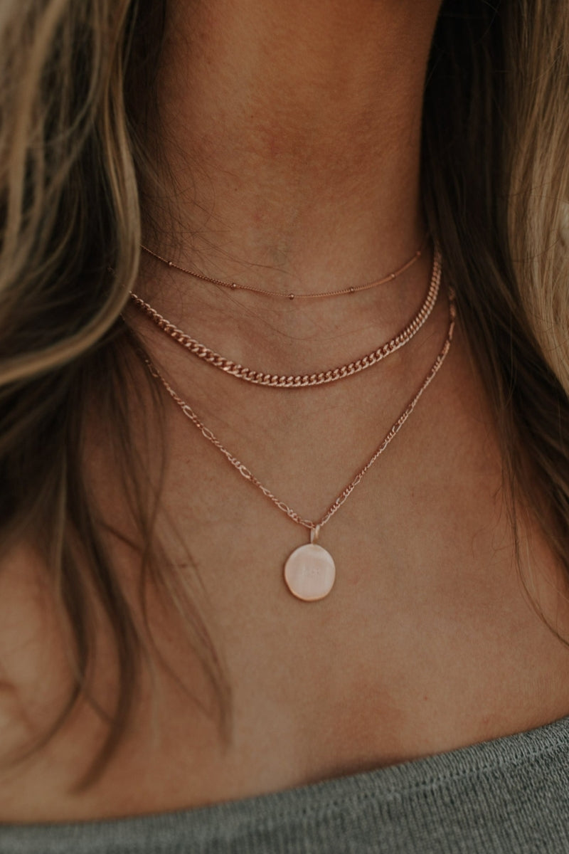 Close-up of engraved rose gold necklace worn with two other delicate gold chains
