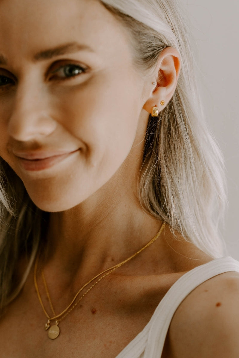 Layered gold necklaces worn together, featuring engraved petite pendant and heart pendant.