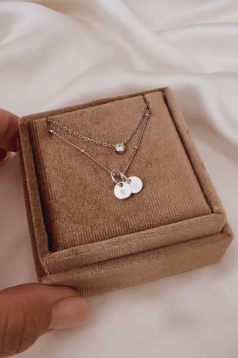 A Silver Lume Necklace sits in a gift box with a Petite Personalised Necklace with two persojnalised initial pendants.  The two necklaces compliment each other and offer a lovely layered necklace look.