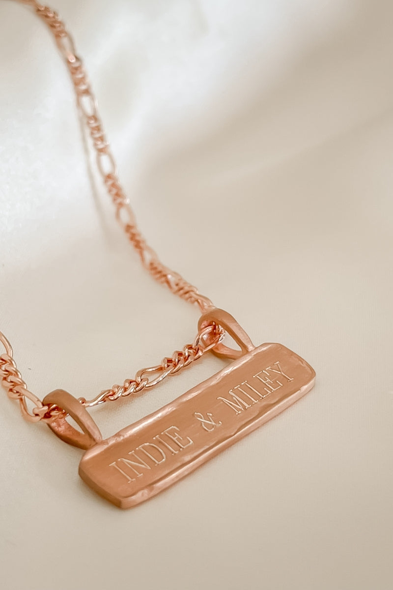 Engraved Signature Bar Necklace in rose gold featuring names. Elegant flatlay of custom pendant with figaro chain.