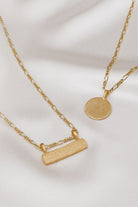Flatlay of gold Signature Necklace and Bar Necklace with engraved names on soft satin backdrop, showcasing timeless design.