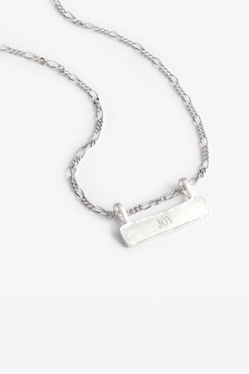 Engraved Signature Bar Necklace Silver featuring the word "JOY" on a figaro-style chain. A timeless, handcrafted sterling silver keepsake.