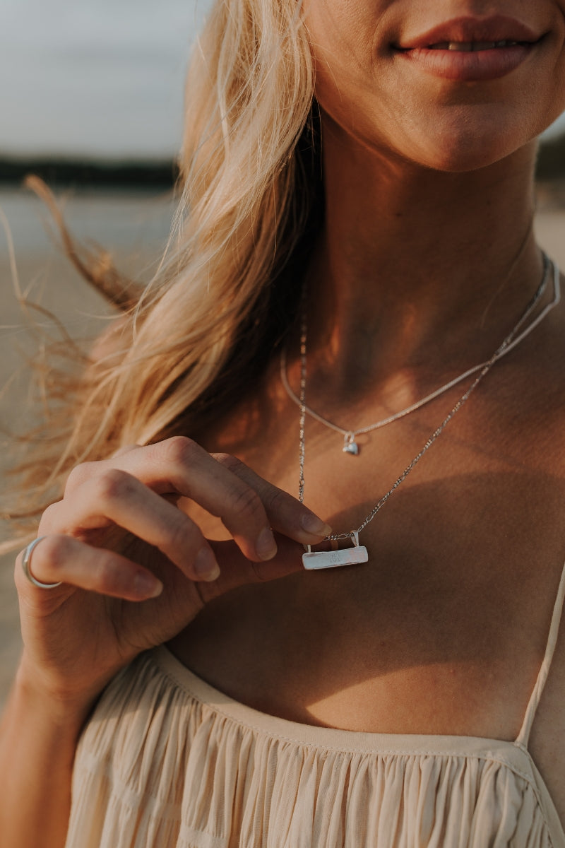 Woman gently holds the Signature Bar Necklace Silver, engraved with a name. A personalised sterling silver gift with heirloom appeal.