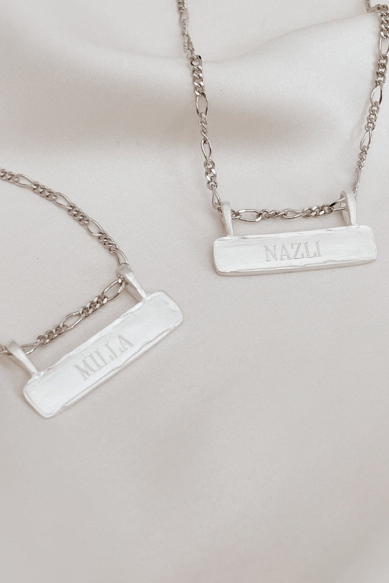 Signature Bar Necklace Silver shown in a flat lay, engraved with “MILLA” and “NAZLI”. A beautiful silver necklace gift for two.