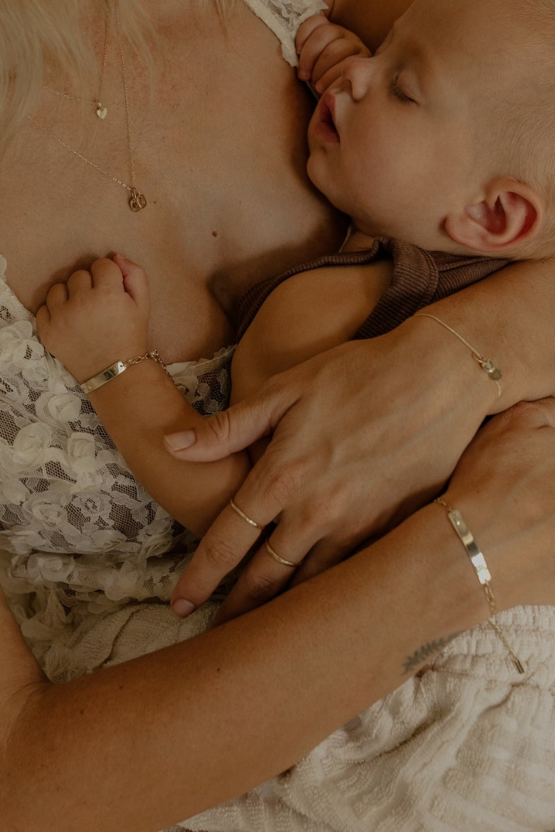 Sleeping baby and mum wearing matching solid gold Darling Bracelets with engraved keepsake plates by Bluebird Jewellery