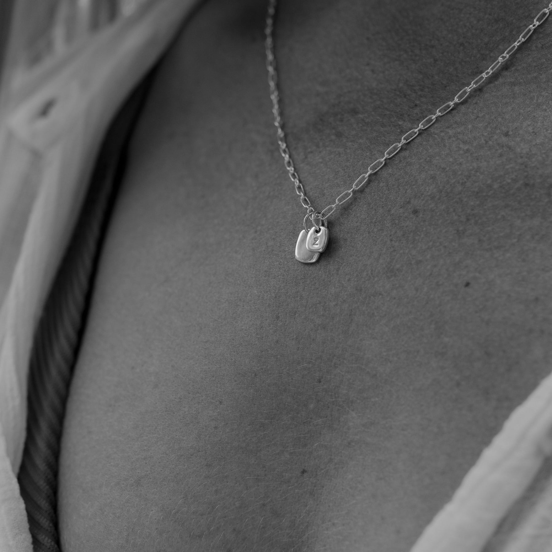 A close up image of a Rectangular Pendant necklace with a regular and mini sized solid sterling silver rectangular pendant rests upon a woman's neck. The mini rectangular pendant is hand stamped with the woman's initial.