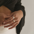 A young woman wears a plain signet ring in size 7 on her pointer finger with a Vintage Pearl Signet Ring worn on her middle finger in a size.