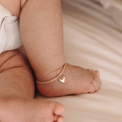 A newborn baby wears a baby length Sweetheart lace chain anklet with a regular sized sweetheart pendant on it.