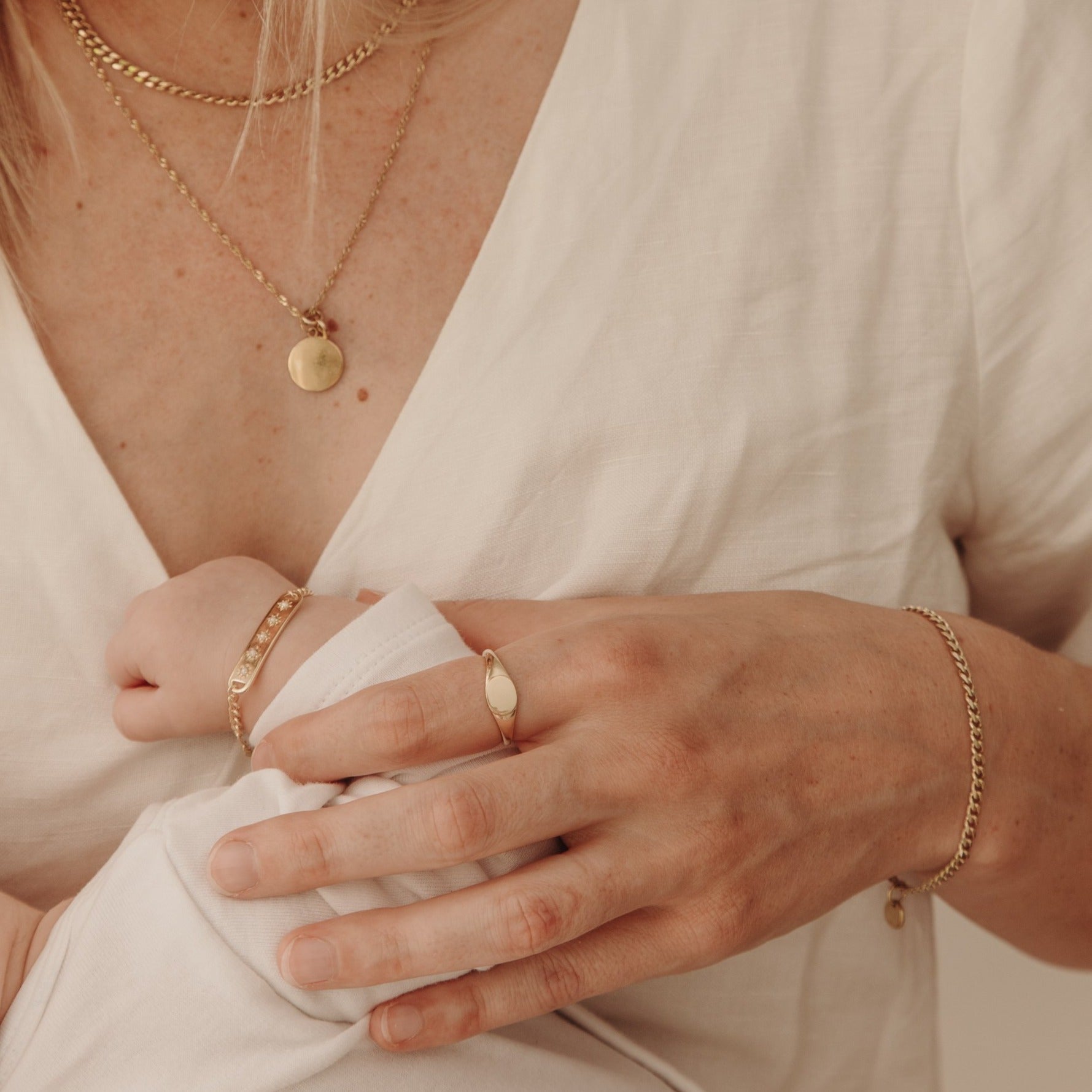 A woman holding her newborn baby is wearing a solid gold signet ring.