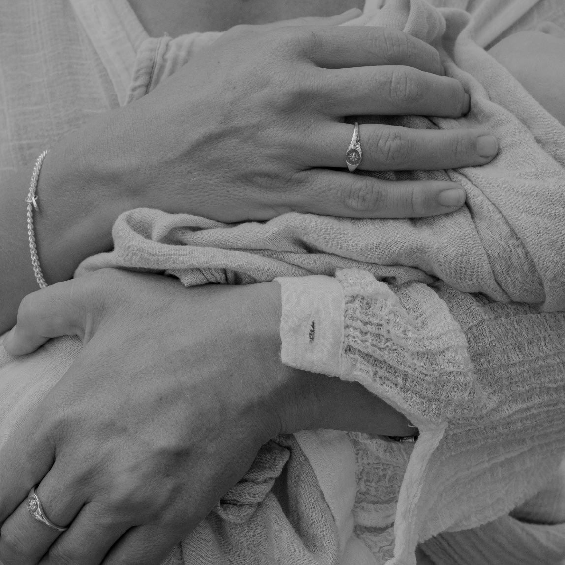 A mother wears a Vintage Pearl Signet Ring on her ring finger as she holds her newborn baby.