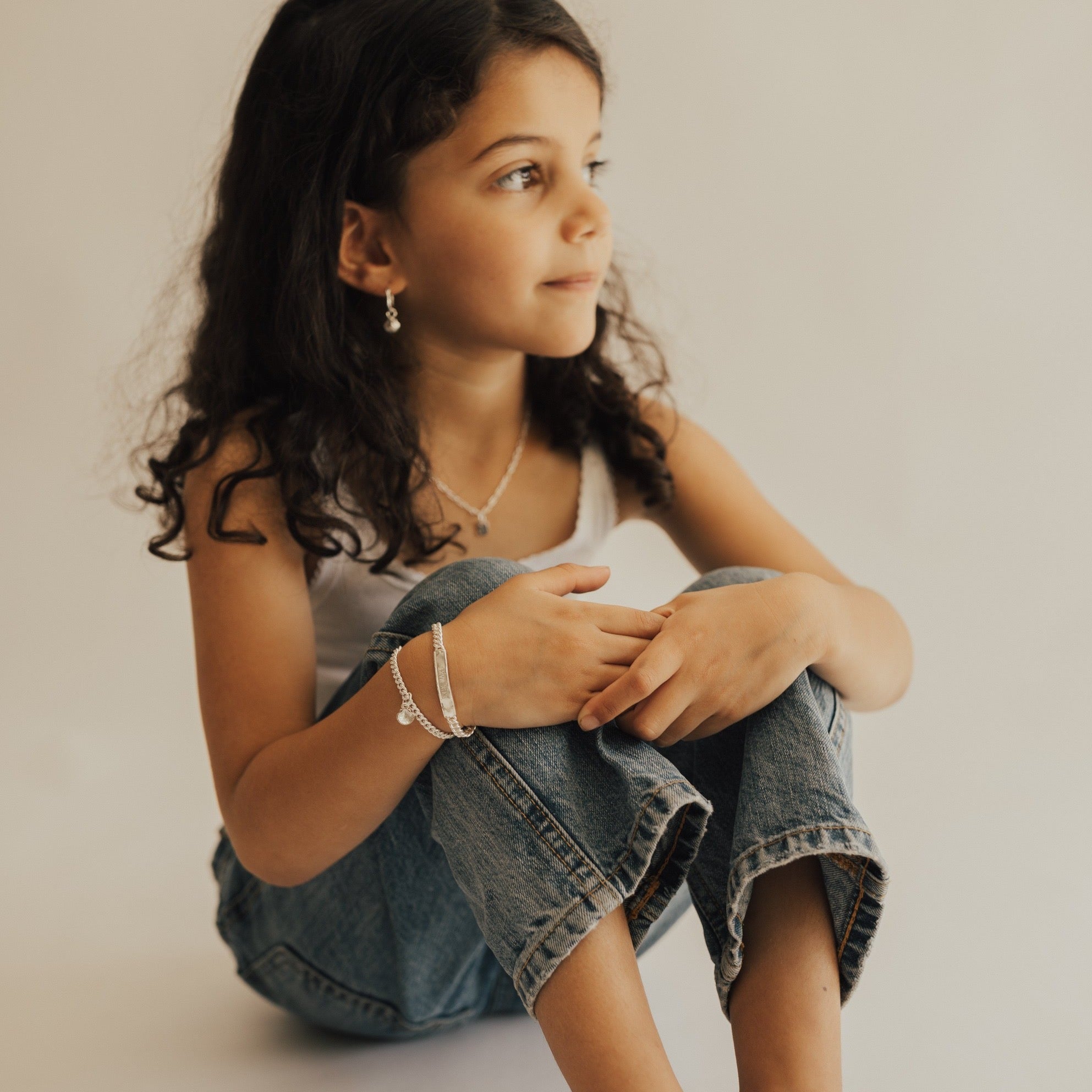 A young girl is wearing the Signature Bracelet in Child size alongside her Little Mermaid Bracelet.