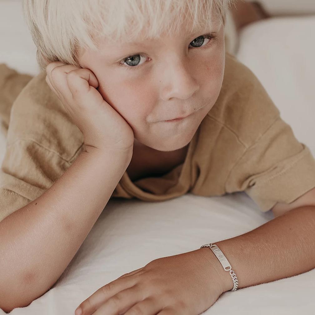 A boy wears his Classic ID bracelet that is a keepsake bracelet made from solid sterling silver.  His name is engraved on the front of the pendant, making it a personalised keepsake bracelet.  He wears the child length adjustable bracelet.