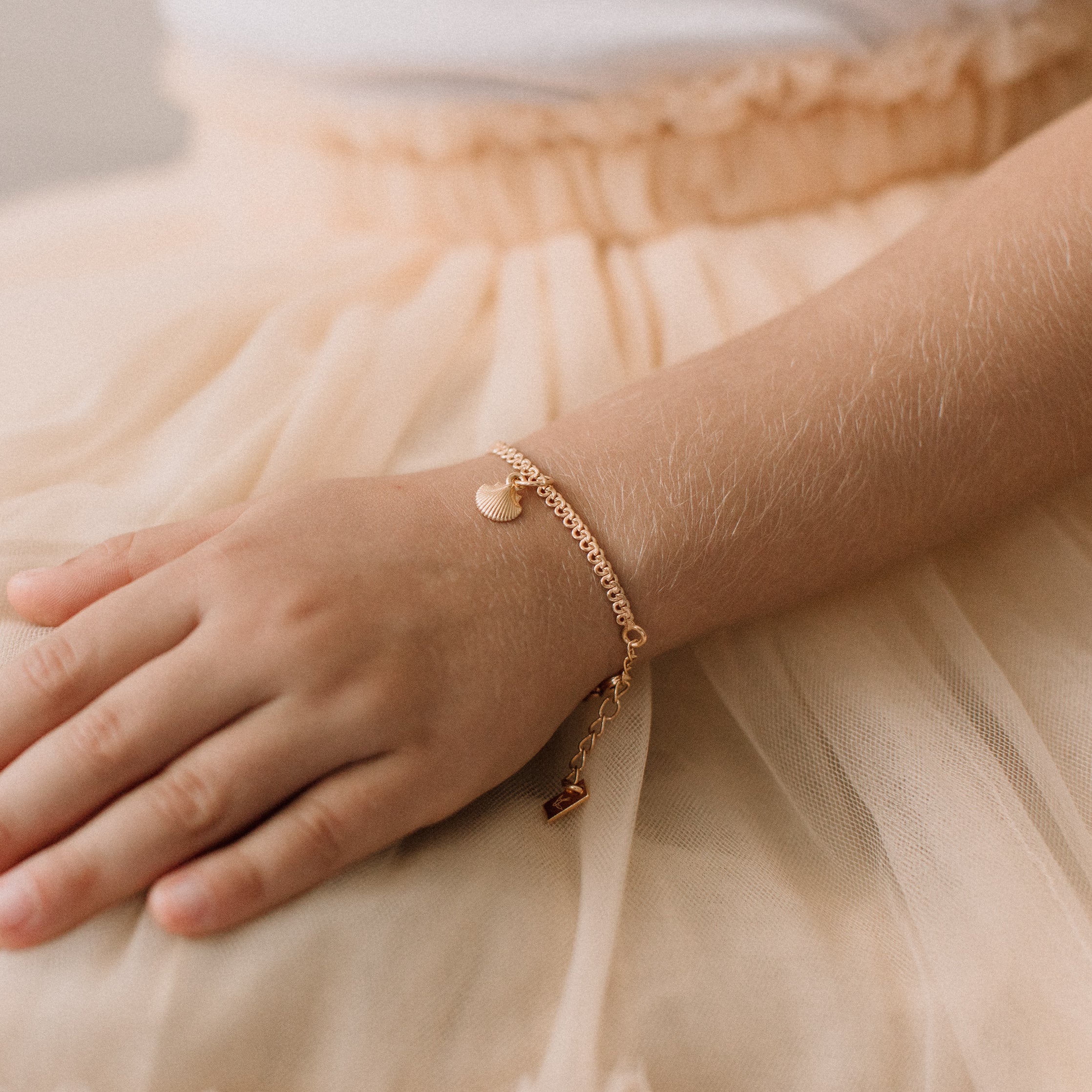 A child wearing a delicate gold Lace Chain bracelet featuring a mermaid shell charm, crafted as a timeless keepsake by Bluebird Jewellery