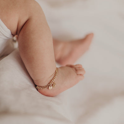 An adorable gold vermeil cuban link chain worn as a baby anklet on a newborn baby's ankle.  The anklet also has a vintage pearl pendant and a solid gold initial pendant.