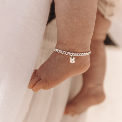 A newborn sized anklet hangs on newborn baby's ankle.  