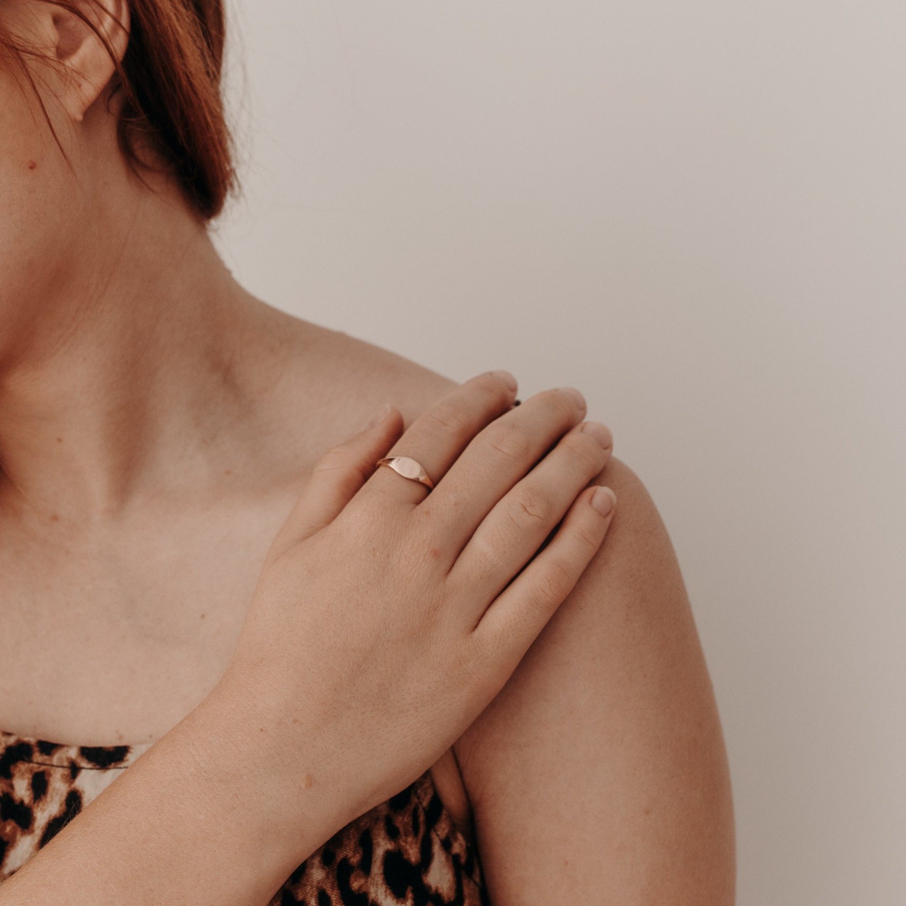 A woman's hand rests elegantly on her shoulder.  The woman is wearing a solid 9ct rose gold signet ring.